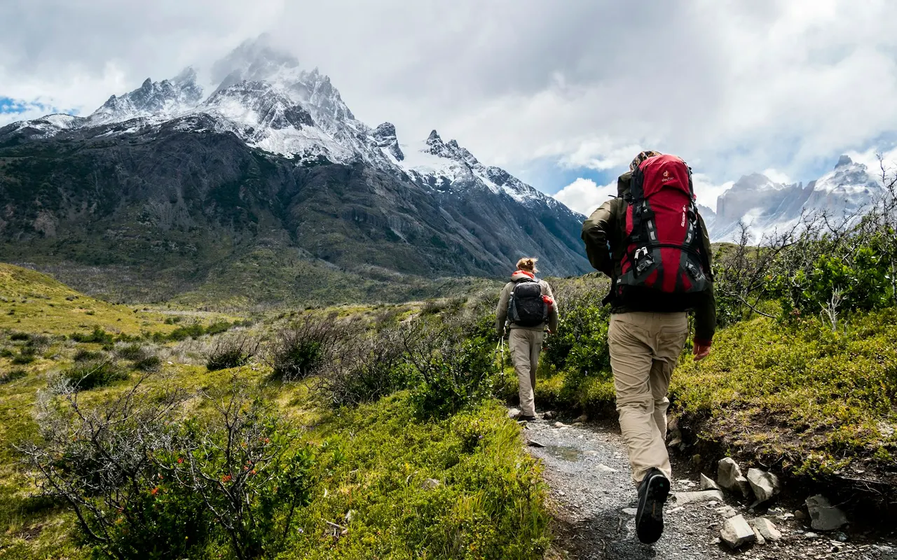 Hikers with backpacks on a trail toward snowy mountains